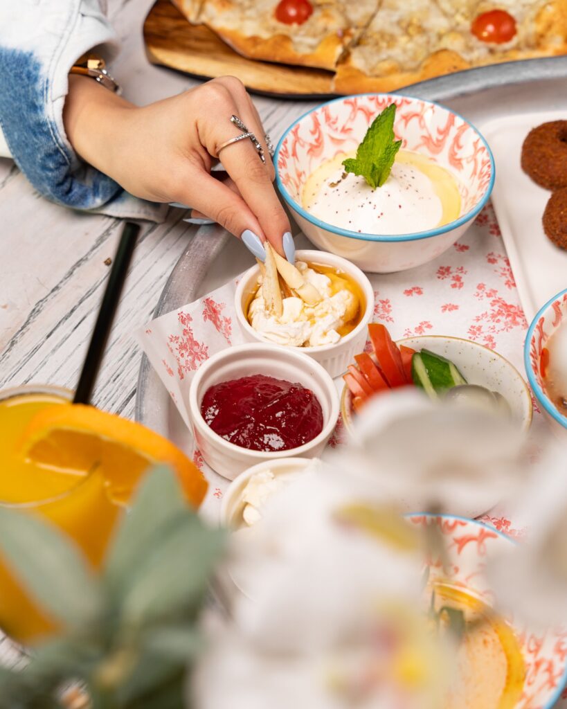 Close-up of a hand dipping bread into sauces, surrounded by a variety of delicious brunch items.